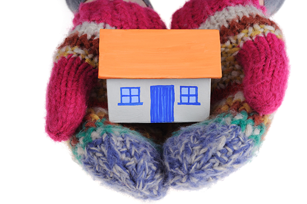 A cardboard house held by hands in mittens