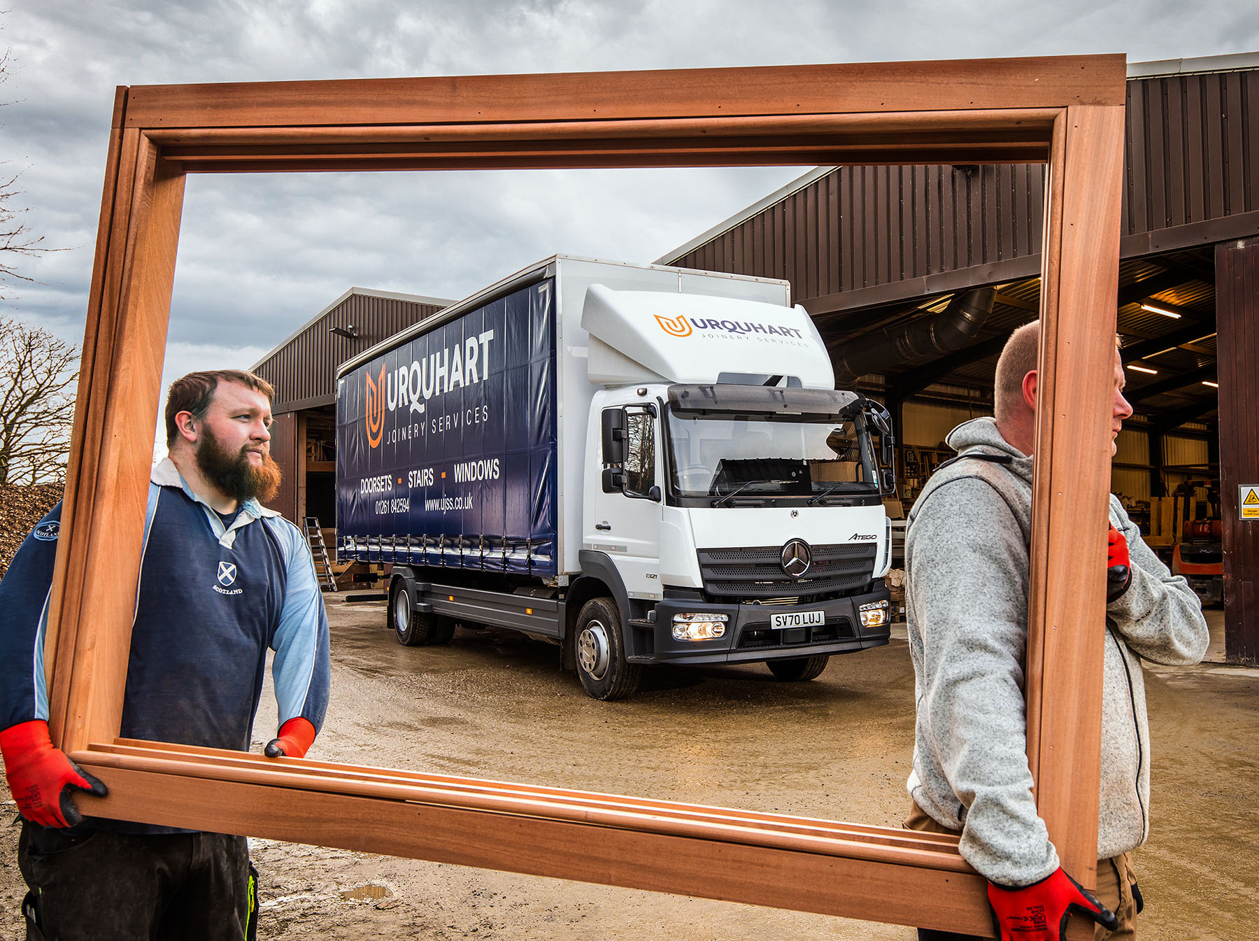 2 man carrying a window frame with a truck in the background