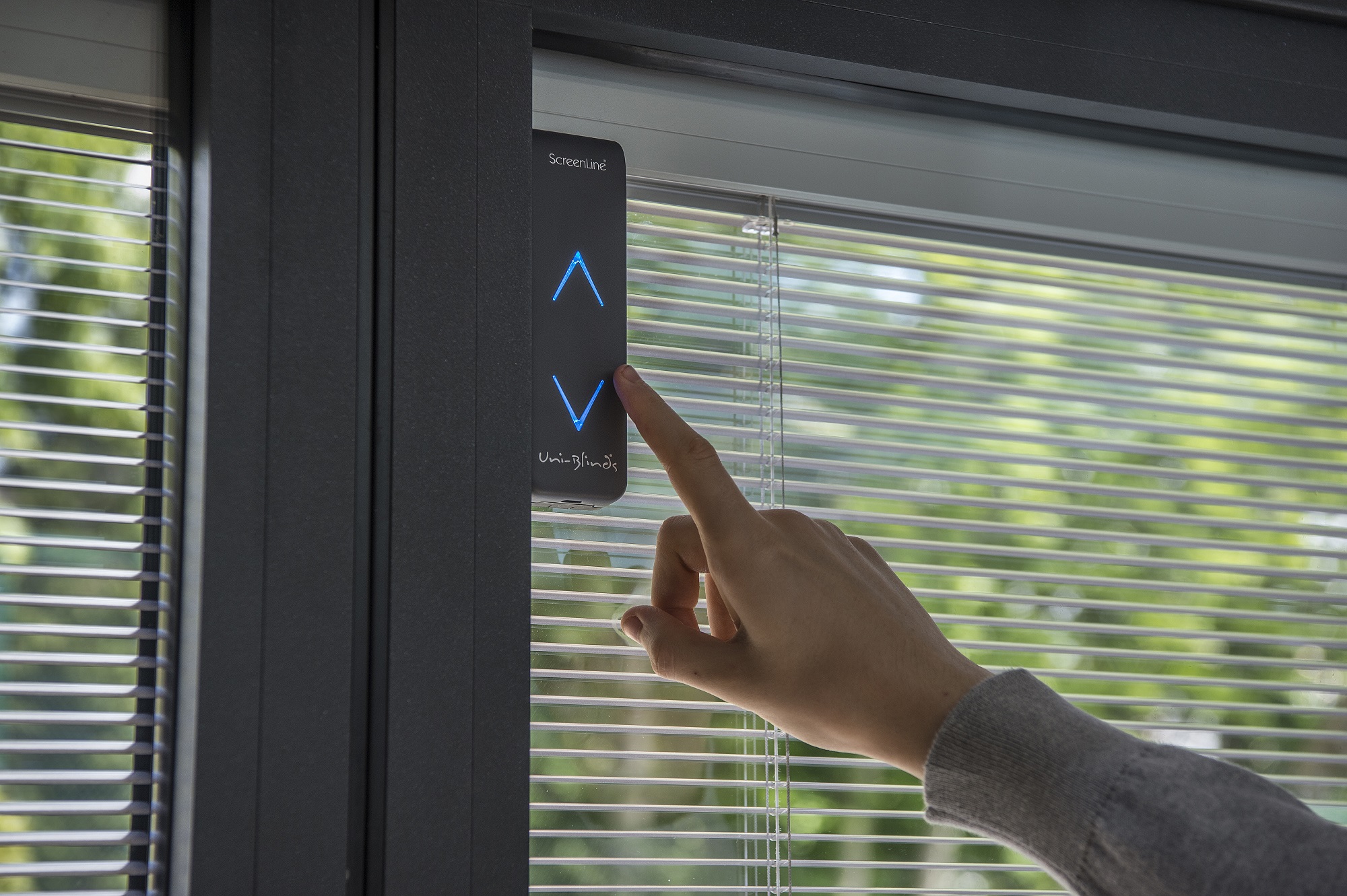 Hand pointing to the control button on W Smart solar controlled blinds.